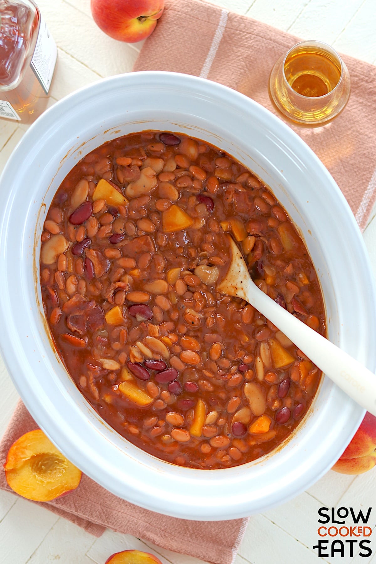 Peach bourbon baked beans crockpot recipe in a white oval slow cooker.