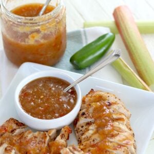 Slow cooker rhubarb sweet chili jam in a white bowl with a spoon and served over sliced grilled chicken.