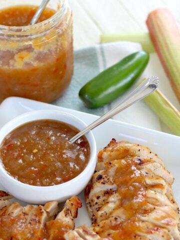 Slow cooker rhubarb sweet chili jam in a white bowl with a spoon and served over sliced grilled chicken.