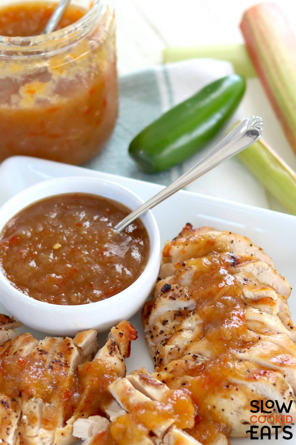 A white bowl of rhubarb sweet chili jam slow cooker recipe served over sliced chicken.