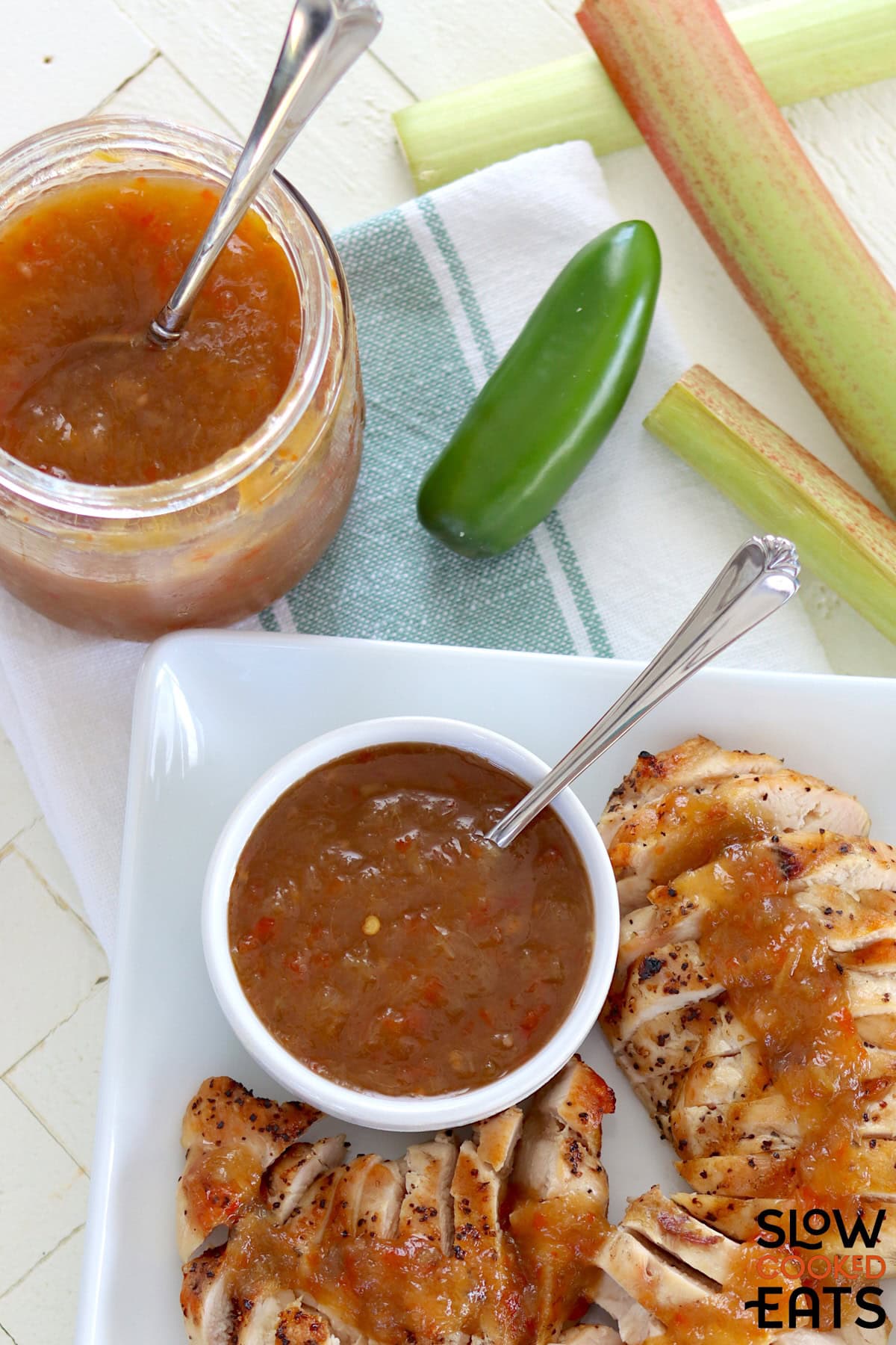 Crockpot rhubarb sweet chili jam in a clear glass jar and a white bowl with a spoon.