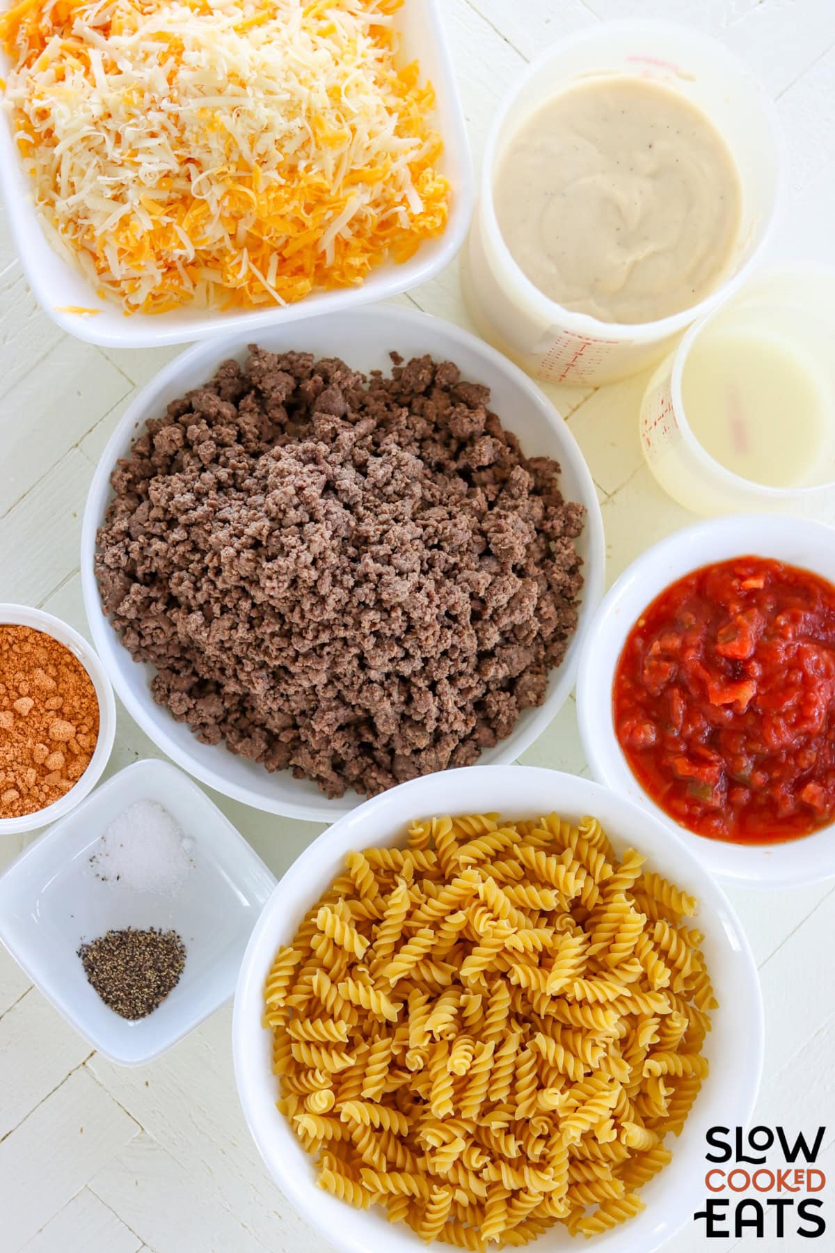 Ingredients needed for making crockpot taco pasta bake on a white wooden board.