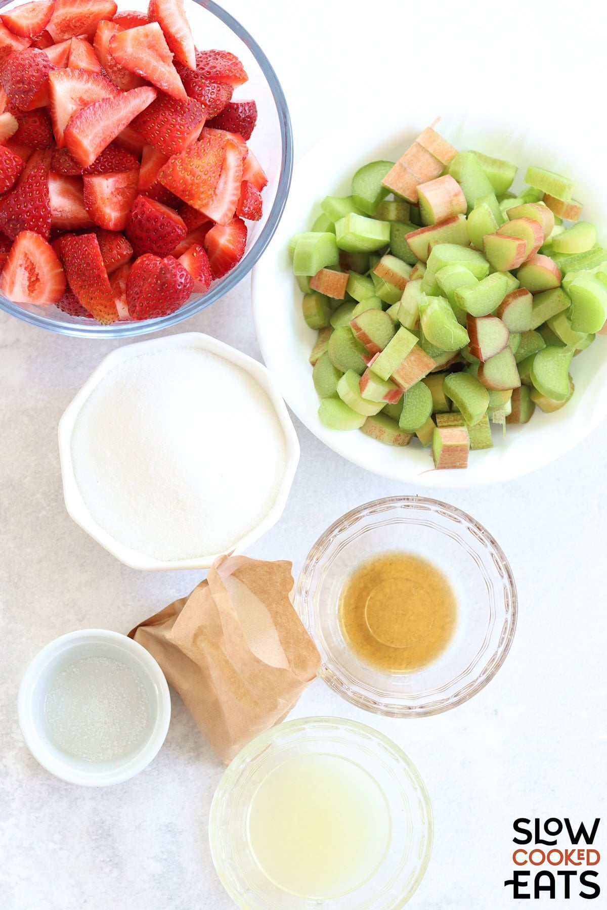 Ingredients for making strawberry rhubarb jam crockpot recipe on a white board.