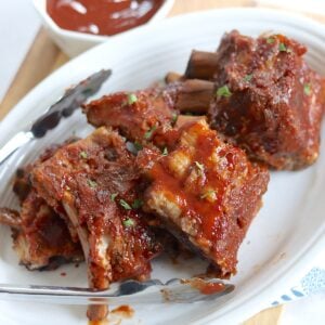 Sections of crockpot baby back ribs slathered with barbecue sauce on a white plate.