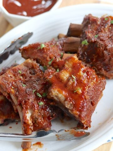 Sections of crockpot baby back ribs slathered with barbecue sauce on a white plate.