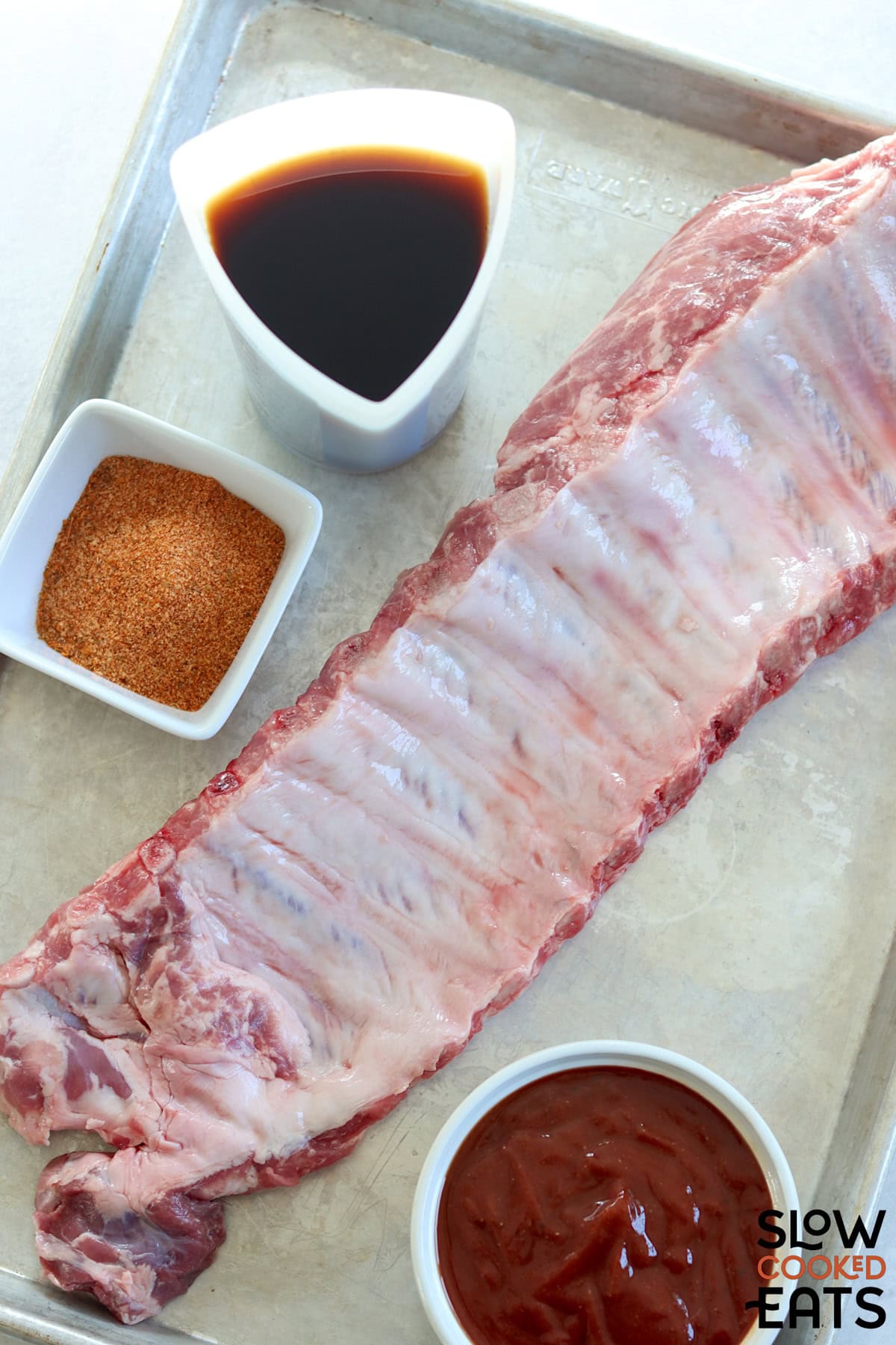 Four ingredients needed to make crockpot Dr Pepper ribs on a metal baking sheet.