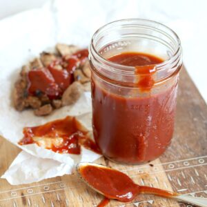Crockpot BBQ sauce in a clear mason jar with a side of sliced chicken.
