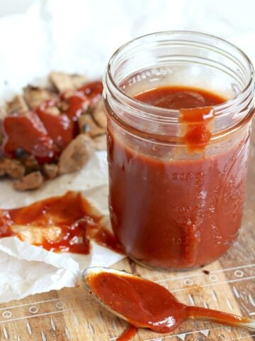 Crockpot BBQ sauce in a clear mason jar with a side of sliced chicken.